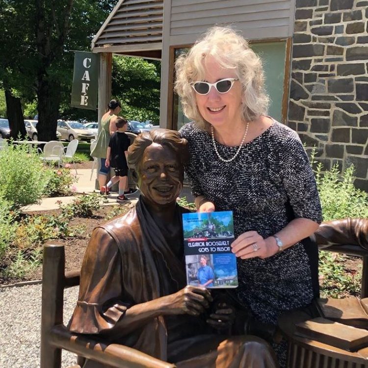 Kathryn Smith sitting with Eleanor Roosevelt statue at the FDR Library holding the book "Eleanor Roosevelt Goes to Prison"