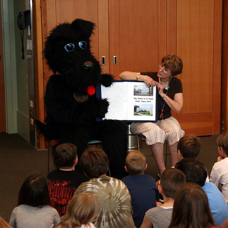 Fala costumed character presenting with a FDR Library staff member to a group of young children