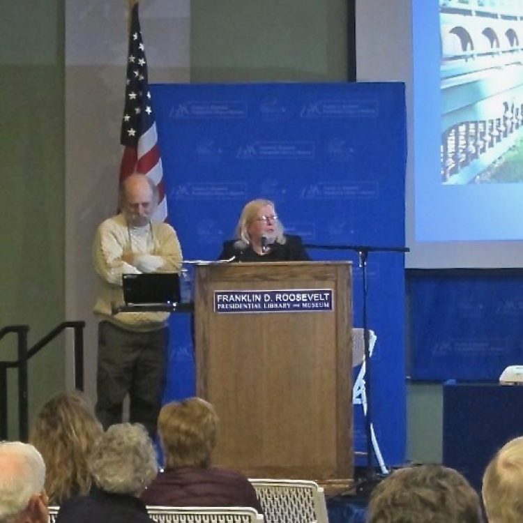 Johanna and Robert Titus, two individual standing behind a podium and in front of a projection screen speaking at an event at the FDR Library.