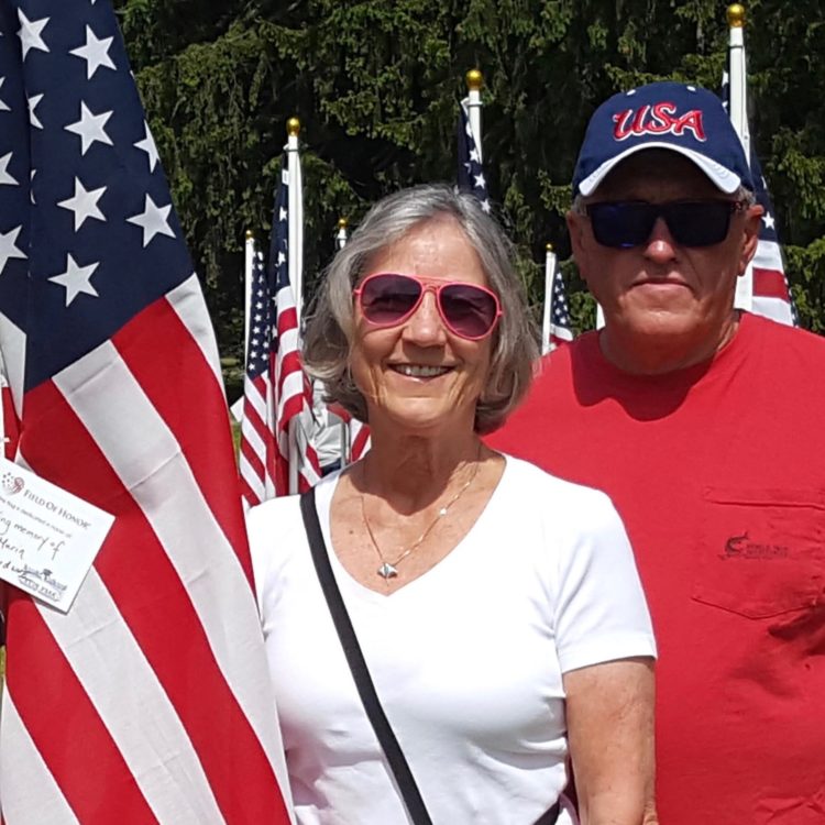 Merrilee Osterhoudt, a white woman, poses with a man wearing a "USA" hat standing next to an American flag