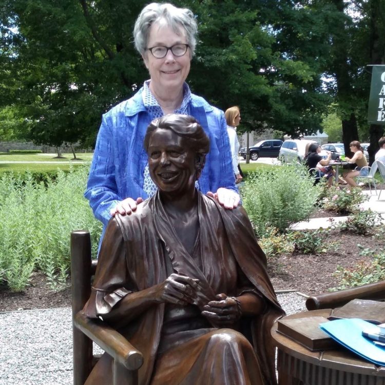 Emily Herring Wilson, a white woman wearing a blue shirt, stands behind a statue of Eleanor Roosevelt at the FDR Library