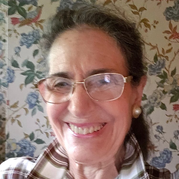 Ellen Danziger, a Library donor, wears glasses and a plaid shirt in front of a floral background