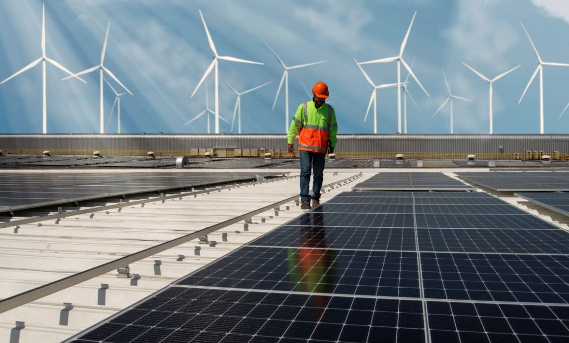 Man checking solar panels with windmills in the background