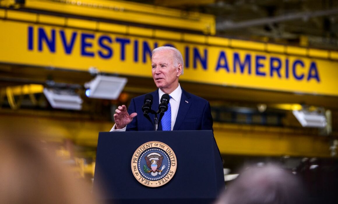 President Biden addressing a crowd in front of an "Invest in America" sign.
