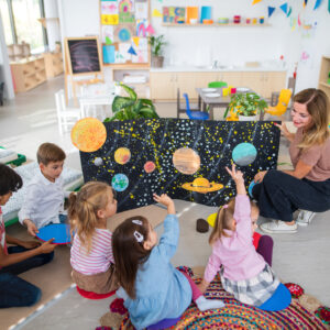 High angle view of pre school teacher showing poster with planets to children indoors in nursery, Montessori education.