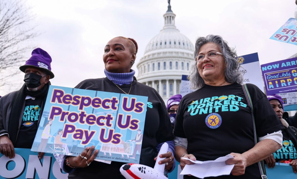 WASHINGTON, DC - DECEMBER 08: Airport workers hold up signs during a press conference held by airport workers and members of SEIU to ask congress to pass the "Good Jobs for Good Airports Act" on Capitol Hill on December 08, 2022 in Washington, DC. (Photo by Jemal Countess/Getty Images for SEIU)