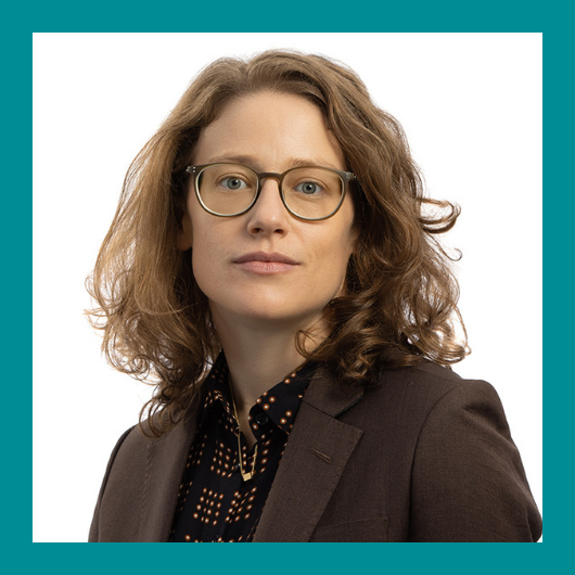 A person with curly light brown hair and glasses wears a dark blazer and patterned shirt, looking confidently at the camera. The image has a teal border.