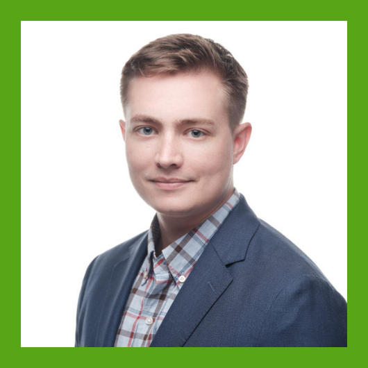A person with short light brown hair wearing a blue blazer and plaid shirt, posing against a white background with a green border around the image.