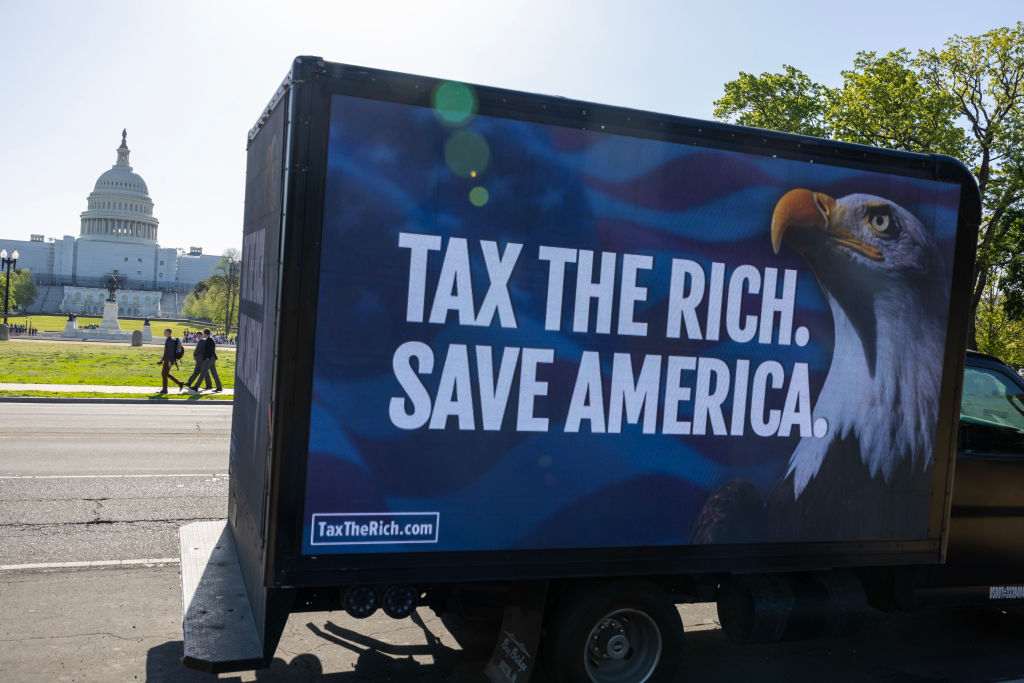 A truck parked near the U.S. Capitol displays a sign with a bald eagle and the words TAX THE RICH. SAVE AMERICA. in large white letters on a blue background.
