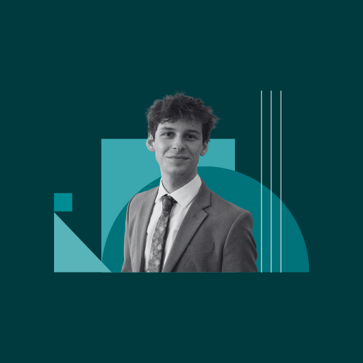 A young man in a suit and tie smiles at the camera. The photo is black and white, with teal geometric shapes in the background.