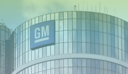The image shows the exterior of a modern glass building with a large blue GM (General Motors) logo displayed near the top.
