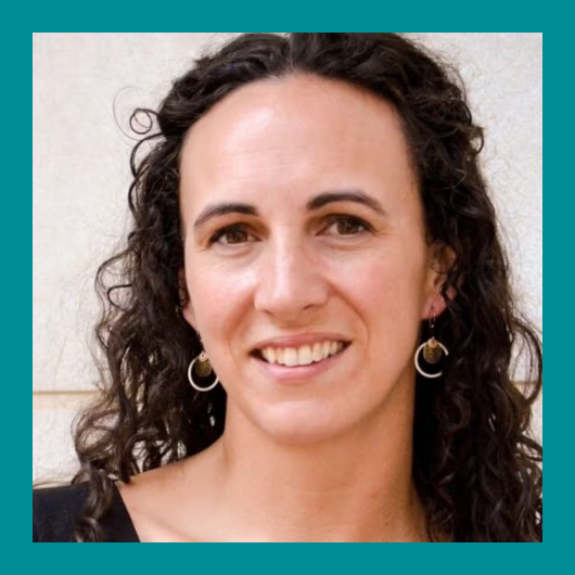 A woman with long, curly dark hair smiles at the camera. She is wearing earrings and a light top, standing in front of a light-colored wall. The image has a teal border.