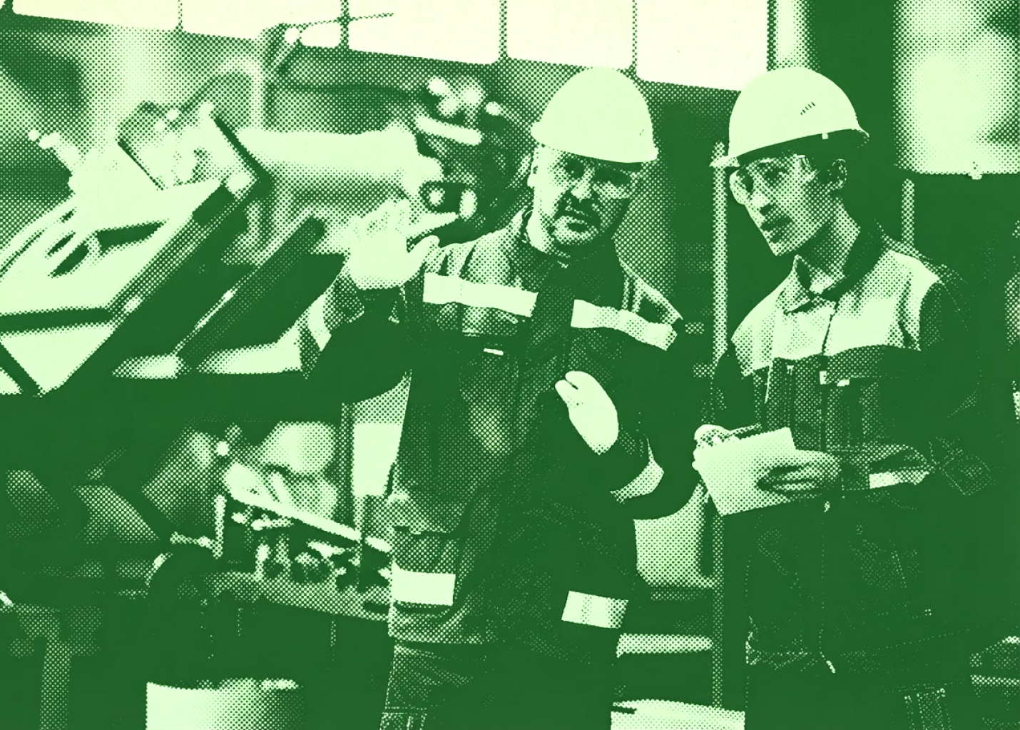Two workers in safety gear and hard hats stand in a factory, discussing something. One gestures with his hands while the other holds a notepad. Machinery and industrial equipment are visible in the background. Image has a green tint.