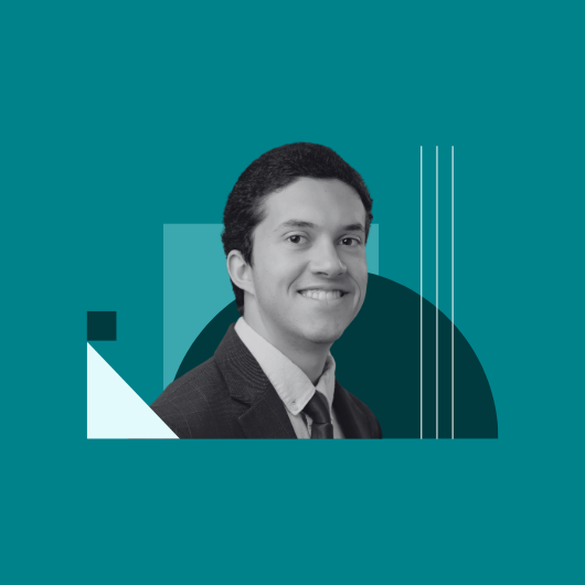 A man in a suit and tie smiles at the camera, with abstract geometric shapes in shades of teal and white in the background.