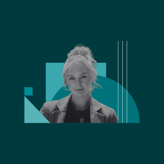 A woman with light hair tied up, wearing a checked blazer, stands in front of teal geometric shapes on a dark teal background.