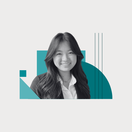 A woman with long hair smiles, wearing a blazer and shirt. Behind her are blue geometric shapes on a white background.