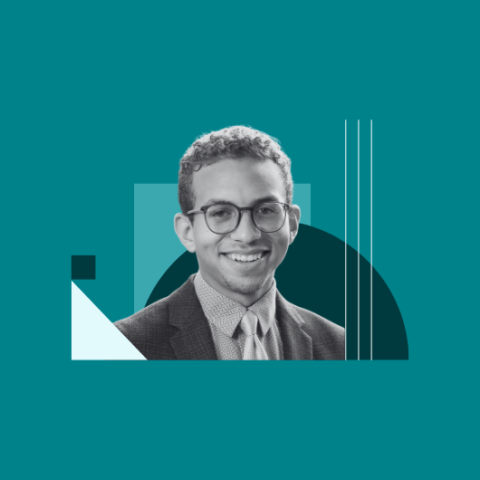 A young man wearing glasses, a suit, and a tie smiles at the camera. The background is teal with abstract geometric shapes in white, black, and teal behind him.