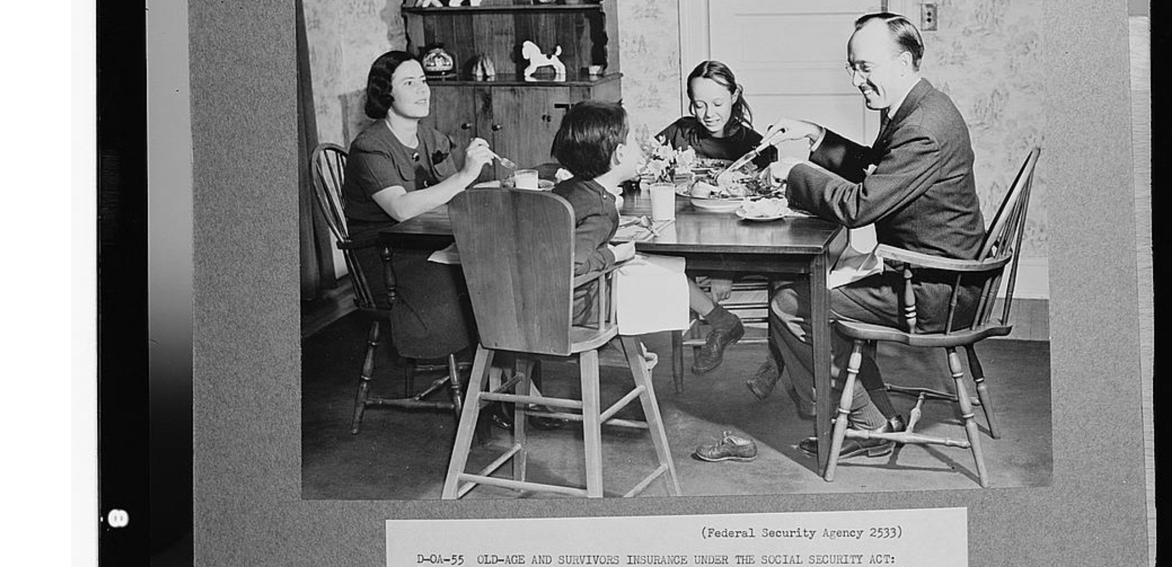 A black-and-white photo of a family of four—two adults and two children—sitting around a dining table, sharing a meal in a modestly decorated kitchen or dining room.