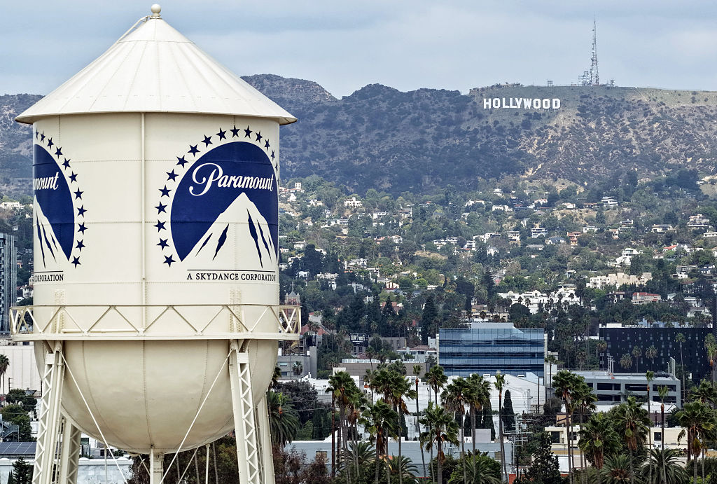 Paramount Pictures water tower in the foreground with the Hollywood Sign visible on the hillside in the background, Los Angeles cityscape below.