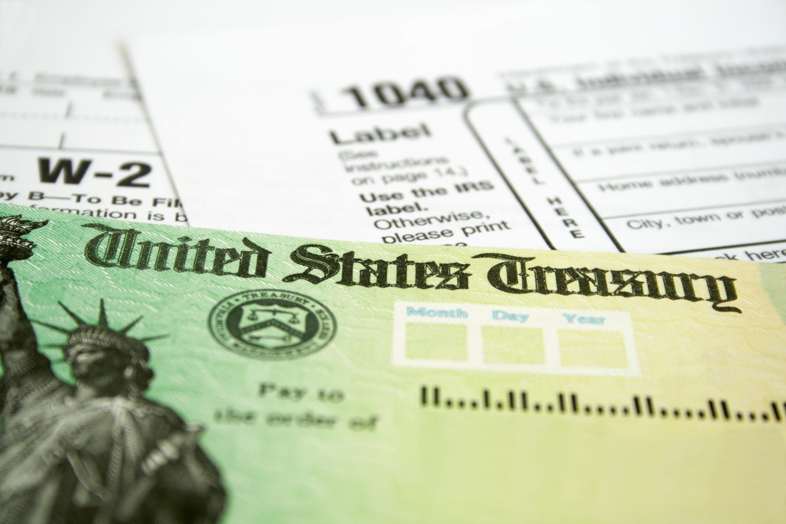 A close-up of a U.S. Treasury check in front of IRS tax forms, including a 1040 form and a W-2 wage statement.