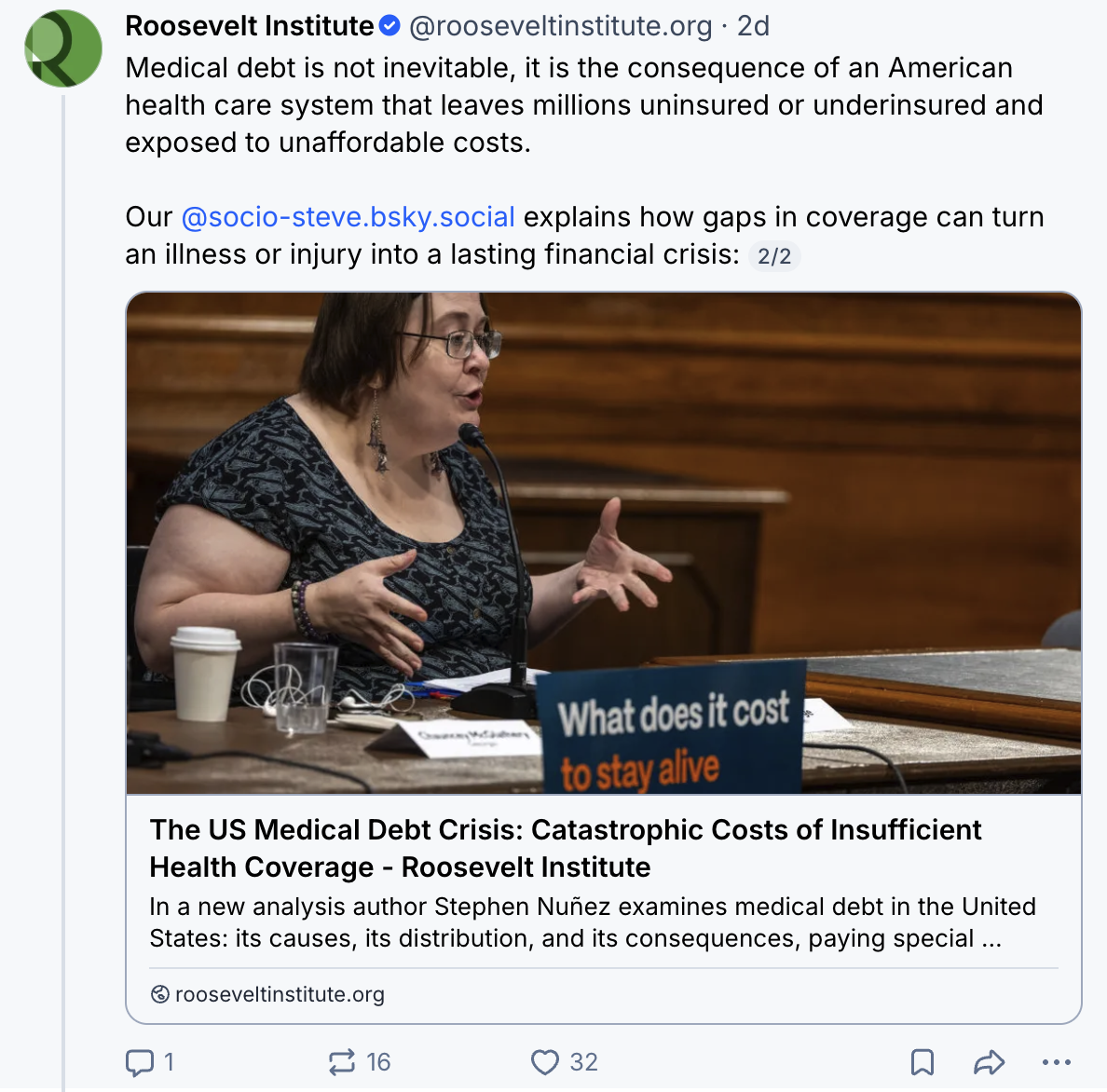 A woman gestures while speaking during a discussion. A sign beside her reads, What does it cost to stay alive. The image relates to a Roosevelt Institute article about US medical debt.