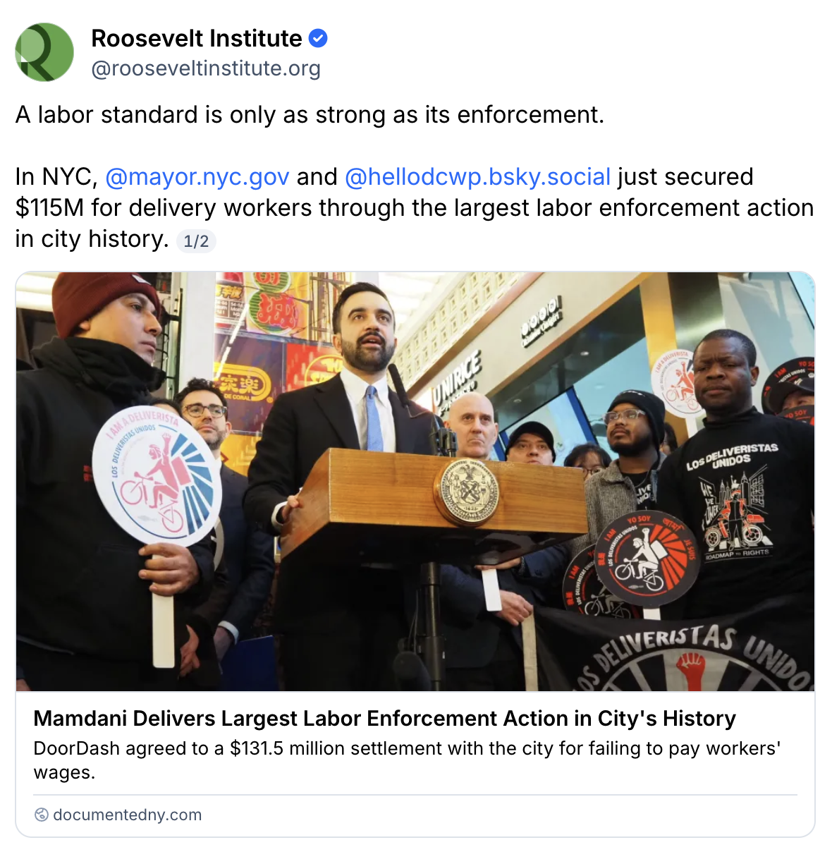 A man in a suit speaks at a podium while delivery workers holding signs stand beside him. A large check for $115M is displayed behind them, showing a major labor enforcement action in New York City.
