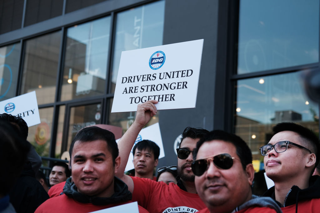 A group of people wearing red shirts hold up a sign that reads, Drivers United Are Stronger Together, featuring the Independent Drivers Guild logo.