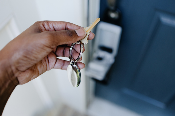 A hand holding a key and a keychain in front of a blue door with a silver lock.